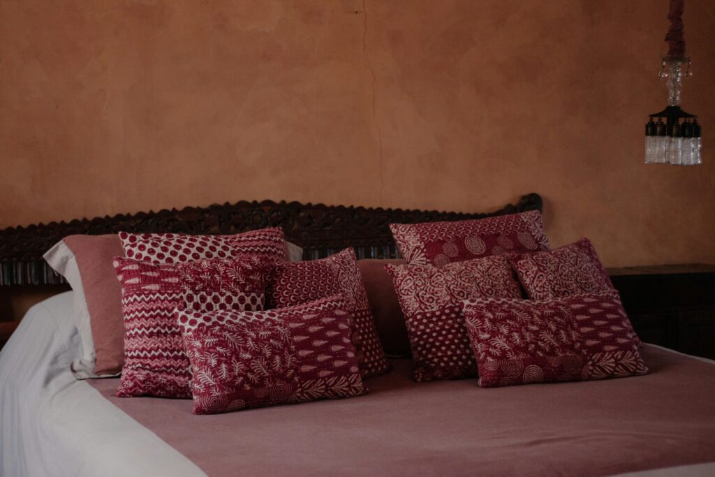 Warm-toned bedroom featuring a bed adorned with patterned red cushions and a classic brown wall.