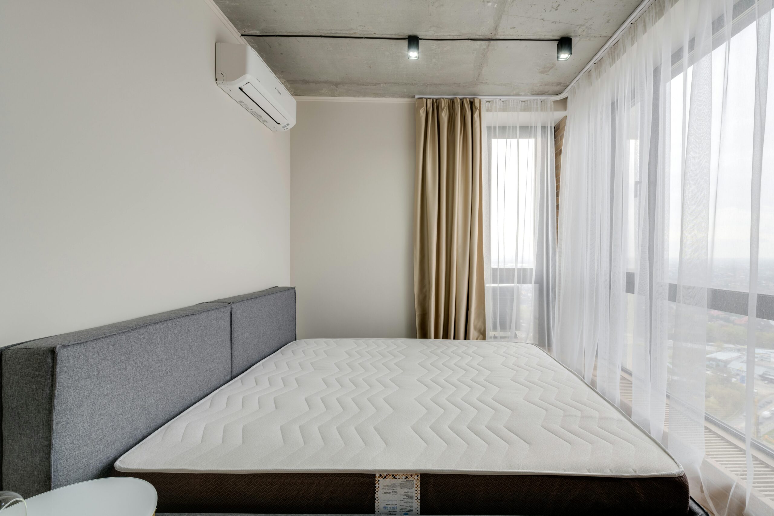 Spacious modern bedroom with a clean mattress and large windows for natural light.